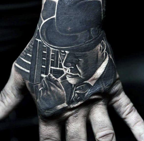 Al Capone tattoo on the hand featuring a black-and-white portrait of the gangster in a fedora, with a serious expression and a finger pressed to his lips.