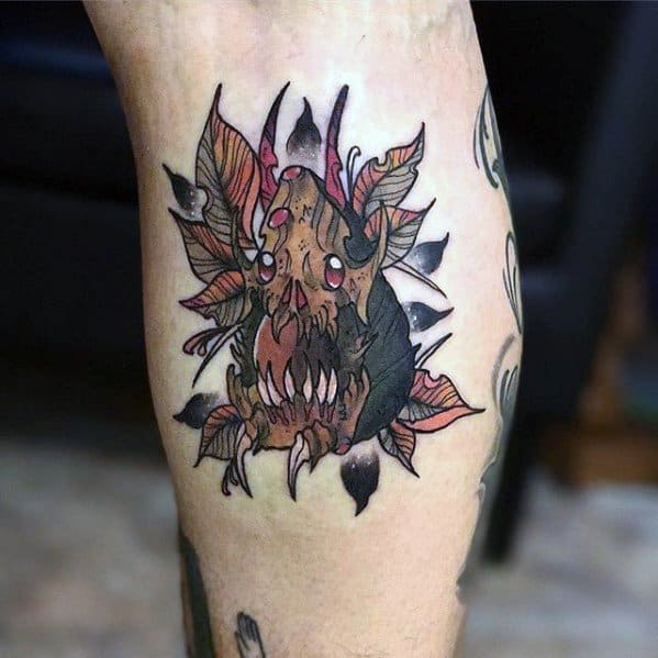 Dark fantasy-style avocado tattoo transformed into a monstrous creature with sharp teeth, horns, and leaves resembling flames.