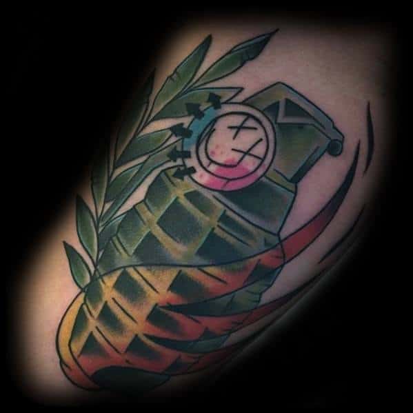 Tattoo featuring a grenade with the Blink-182 smiley face logo on it, surrounded by a laurel branch and colorful flames, creating a bold and dynamic design.