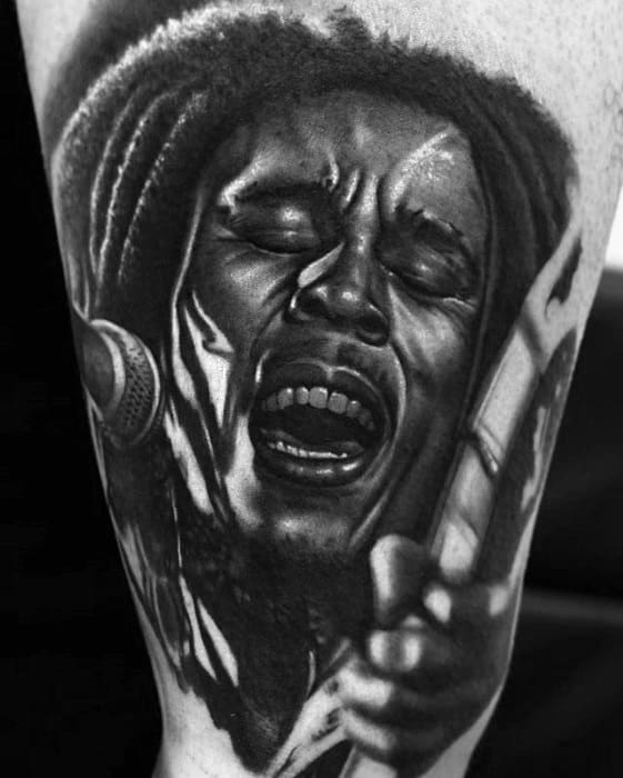 Powerful black and gray tattoo of Bob Marley singing passionately into a microphone, with intense facial expression and detailed highlights.
