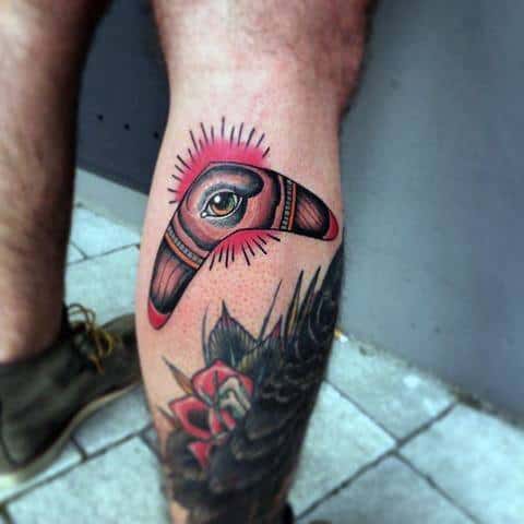 Boomerang tattoo on the calf featuring a central eye, radiating lines, and bold shading for a mystical, watchful effect.