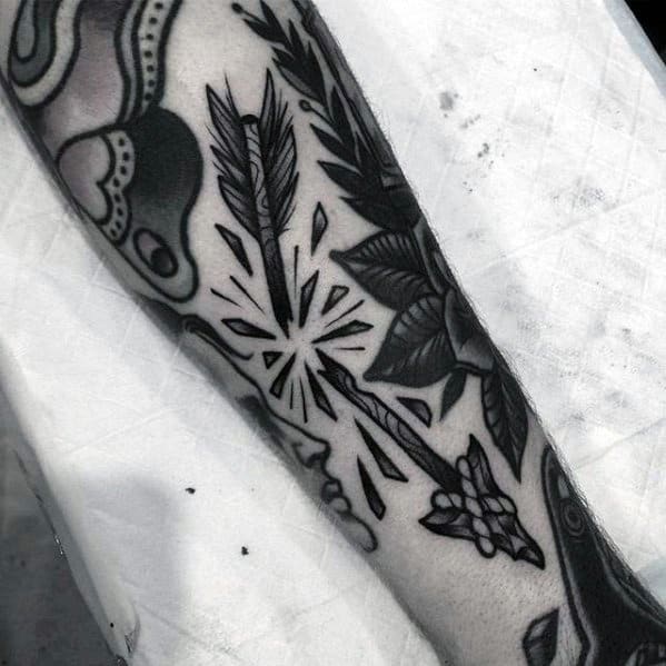 Black and grey tattoo of a broken arrow bursting apart with star-like shards, surrounded by bold floral and traditional filler designs.