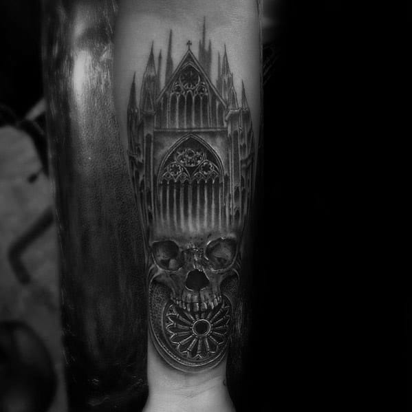 Forearm tattoo of a gothic cathedral merging into a realistic skull, with dark shading and a rose window forming the mouth area.