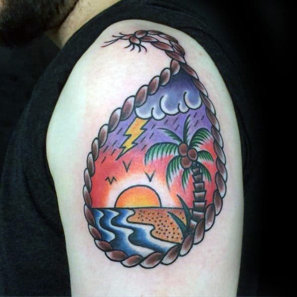 Vibrant upper arm tattoo of a beach sunset scene with a coconut tree, storm cloud, and ocean, framed by a rope-style border.
