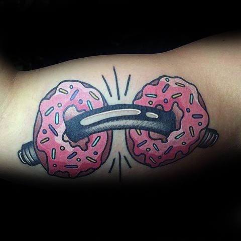 Tattoo of a dumbbell with pink frosted donuts as weights, blending fitness and fun with a playful cartoon style