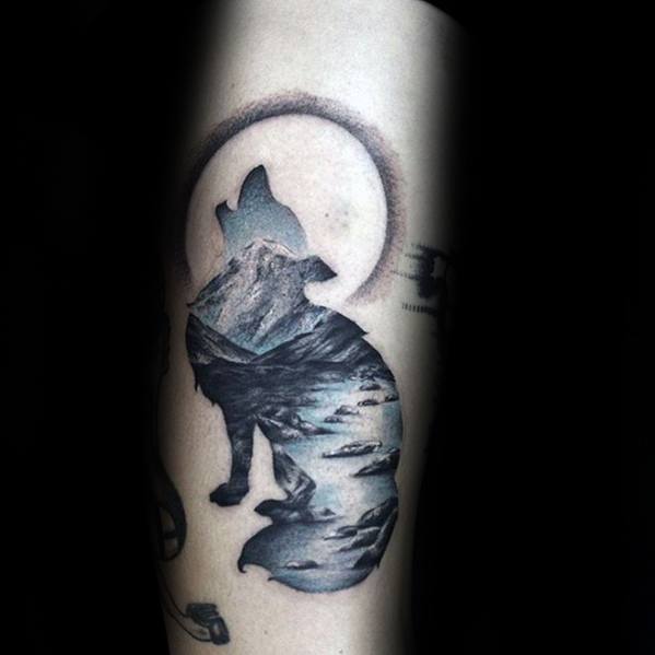 Monochrome tattoo of a howling wolf silhouette filled with a mountain and lake landscape under a glowing moon, symbolizing wilderness and spirit.