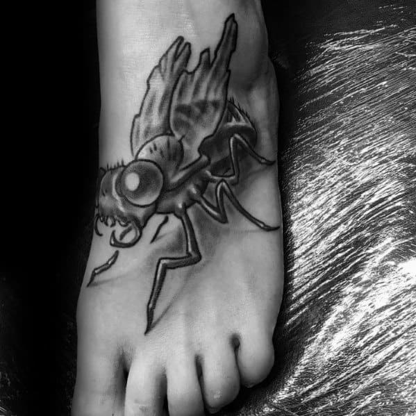 Large black and grey fly tattoo on the foot with bold shading, exaggerated eyes, and dynamic pose for a dramatic, eye-catching design.