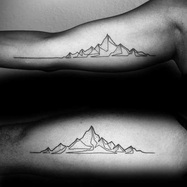 Minimalist mountain range tattoos on the inner biceps, featuring fine line peaks and a continuous horizon line.