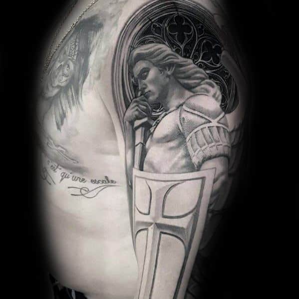 A black and grey tattoo on the side, featuring an angel holding a shield, with a gothic-style window in the background and detailed shading.