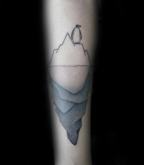 Minimalist iceberg tattoo with a penguin standing on top and layered dotwork shading below the waterline on the forearm.