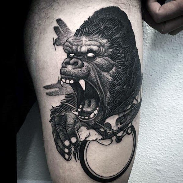 Black and grey King Kong tattoo with bold linework, showing Kong roaring and gripping a broken handcuff while a plane crashes behind him.