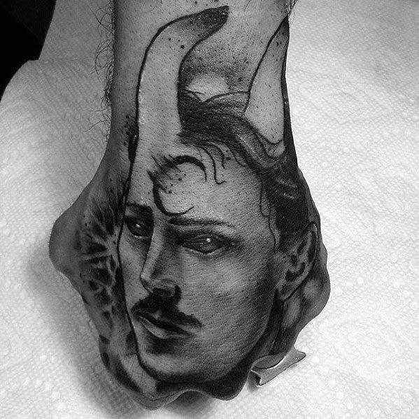Black and grey Nikola Tesla tattoo on the hand with surreal horns, abstract shading, and a mysterious, dreamlike expression.