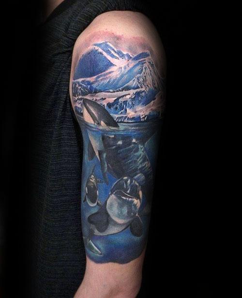 Vibrant and detailed color tattoo on the upper arm, depicting orcas swimming beneath the surface, with a snowy mountain landscape above, creating a breathtaking scene.