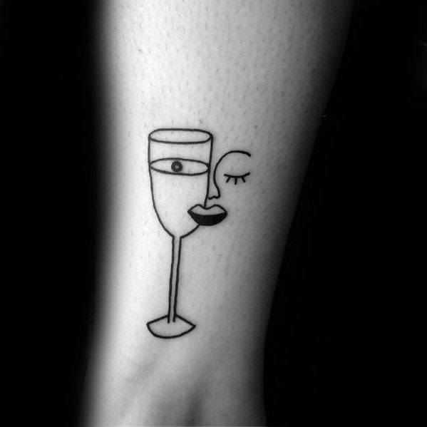 Minimalist Picasso-style tattoo of a wine glass forming a woman’s face, with a single eye, lips, and a closed eyelid.