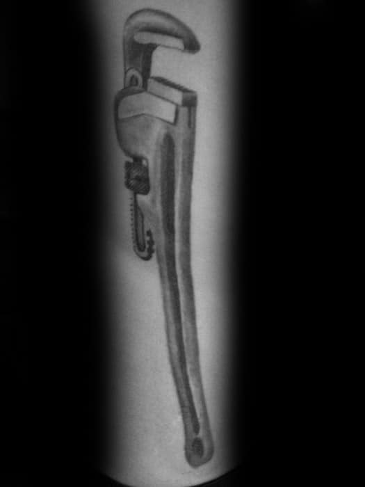 Realistic black and grey tattoo of a detailed pipe wrench, shaded to give a three-dimensional metallic effect.