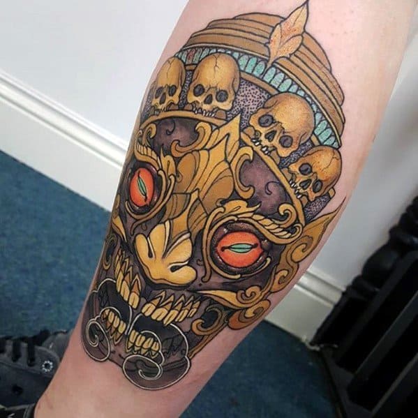Colorful Tibetan skull tattoo on calf with fiery eyes, golden crown adorned with skulls, and ornate swirling patterns.