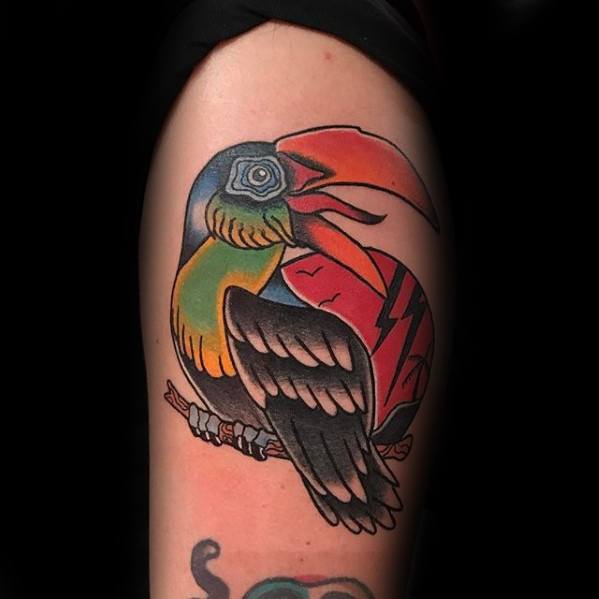 Bold neo-traditional toucan tattoo on upper arm with vibrant colors, stylized eye, and red patterned background for a striking look.