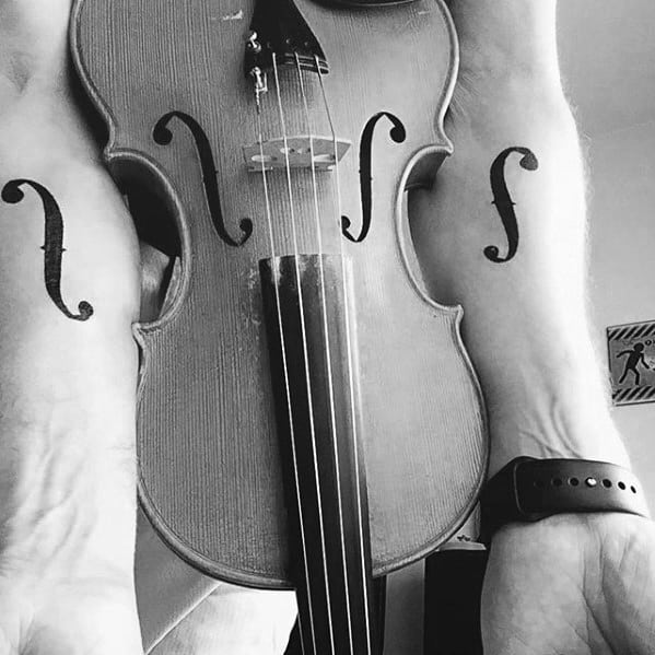 Minimalist black f-hole tattoos on both inner forearms, mirroring the design of a violin placed between the arms for perfect alignment.