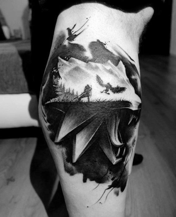 Artistic Witcher tattoo on the calf blending Geralt’s wolf medallion with a mountain scene, forest, and birds in a watercolor style.