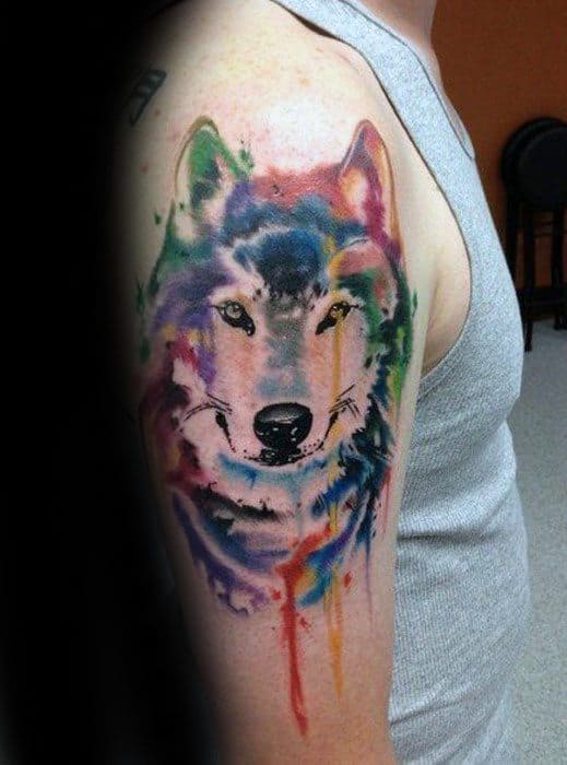 Colorful watercolor wolf tattoo on upper arm with soft blends of blue, purple, red, and yellow, creating a bold yet dreamy look.