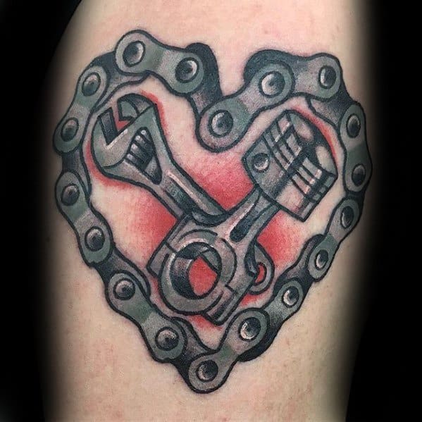 Tattoo of a wrench and piston crossed inside a heart-shaped bike chain, with a red background symbolizing mechanical passion.