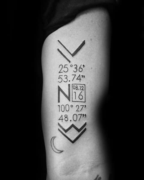 Geometric coordinate tattoo on the upper arm with bold arrows, numbers, and a date box, symbolizing a meaningful place and personal journey.