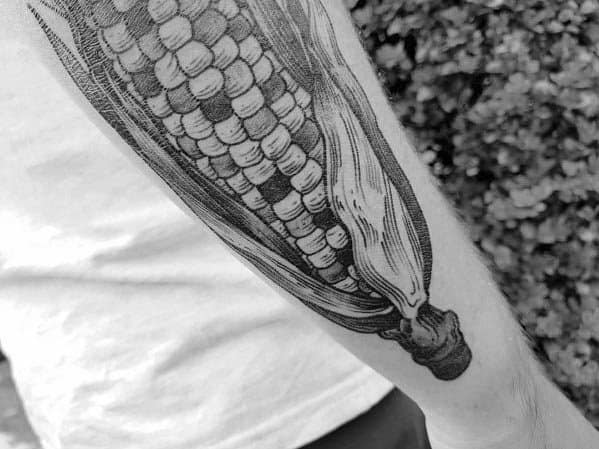 Black and gray tattoo of a realistic corn cob with husks, featuring fine linework and shading for a detailed and textured look.