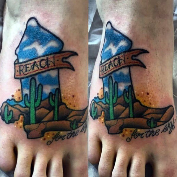 Tattoo of a cowboy boot forming a desert landscape with cacti and mountains, featuring a banner reading "Reach for the sky," symbolizing ambition.
