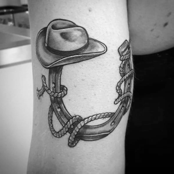 Black and gray tattoo of a cowboy hat resting on a horseshoe wrapped in rope, done in a realistic Western style with fine shading and detail.