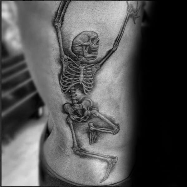 Dancing skeleton tattoo with raised arms and a dynamic pose, shaded in black and gray for a bold and striking ribcage design.
