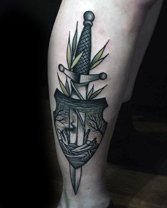 Stylized Dark Souls tattoo of a dagger piercing a shield, with a bonfire and eerie landscape scene framed within, accented by leaves.