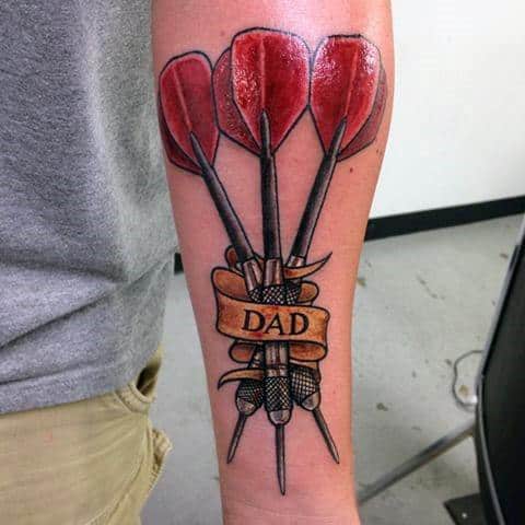Forearm tattoo of five red darts with a banner reading "Dad," combining bold color with a heartfelt tribute to a loved one.