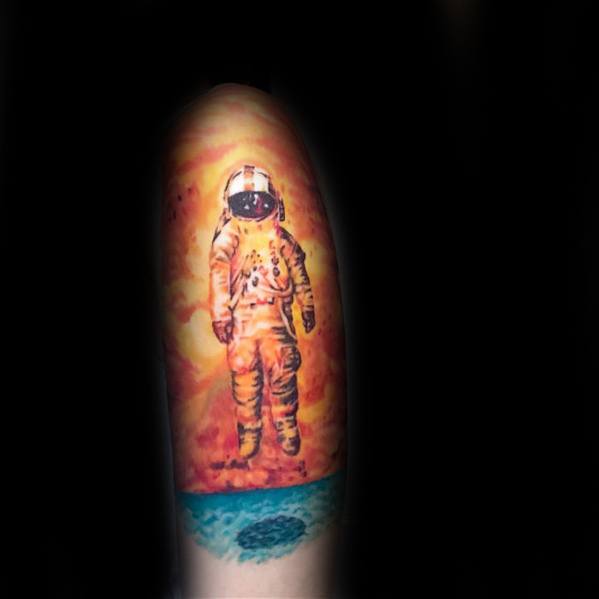 Deja Entendu astronaut tattoo with a fiery orange sky and detailed teal ocean, capturing a vivid, surreal floating moment.