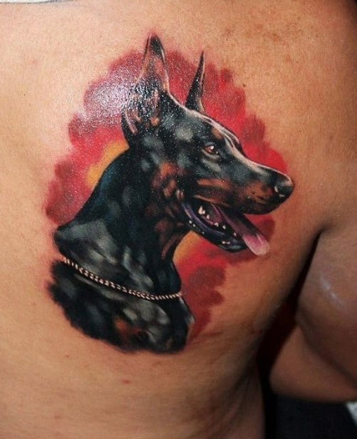 Realistic Doberman tattoo with rich black and brown tones, set against a vivid red and yellow background for a bold, fiery effect.