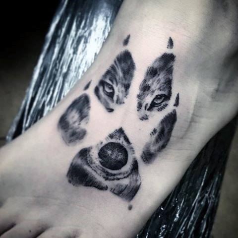 Black and grey tattoo of a wolf's face creatively shaped like a paw print, with intense eyes and a detailed snout.