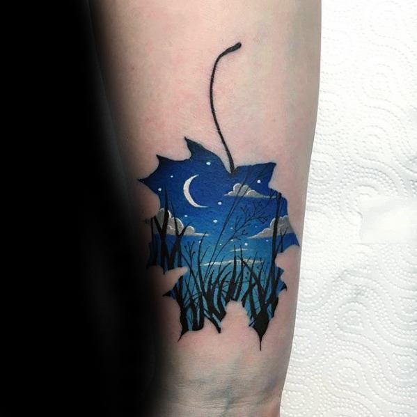 Tattoo of a maple leaf silhouette filled with a serene night scene, featuring a crescent moon, clouds, stars, and tall grass.