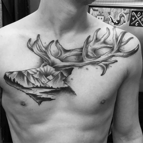 Black and grey elk antler tattoo on the chest, featuring a mountain landscape integrated into the design for a bold and nature-inspired look.