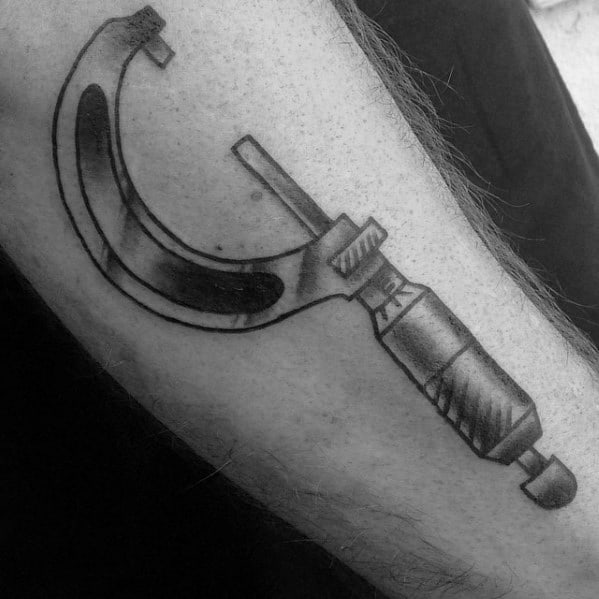 Tattoo of a detailed micrometer in black and gray ink, symbolizing precision and craftsmanship, placed prominently on the forearm.