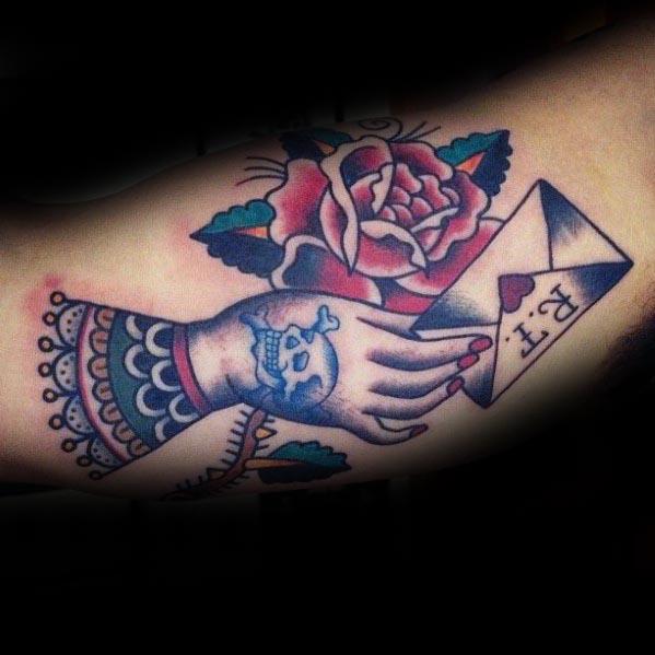 Tattoo of a hand gripping an envelope with a rose, skull, and lace-like details