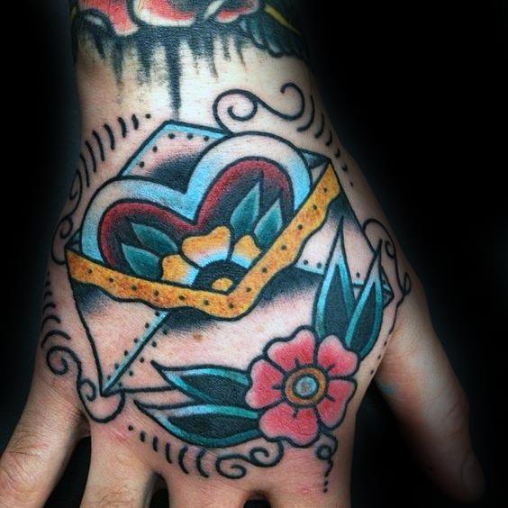 Envelope hand tattoo with a heart, flowers, and decorative patterns