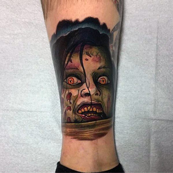 Colorful Evil Dead tattoo of a possessed woman’s head with glowing red-orange eyes, green decaying skin, and eerie expression emerging from the ground