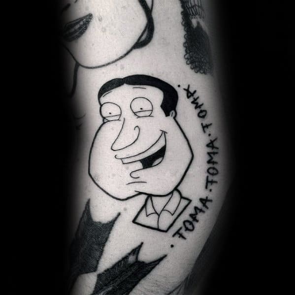 Tattoo of Glenn Quagmire from Family Guy in black ink, featuring his signature grin with the phrase "TOMA. TOMA. TOMA." written beside him.