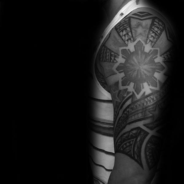 Filipino sun tattoo on the shoulder with tribal rays, bold stars, and dynamic geometric patterns extending into a half-sleeve design.
