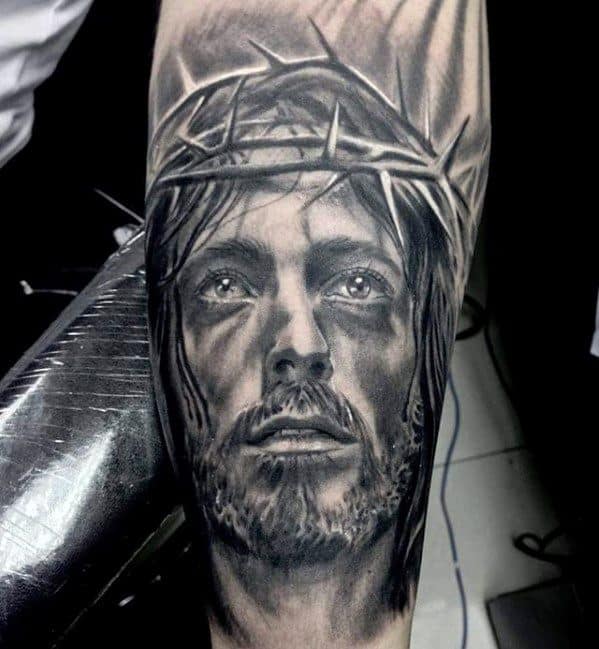 Tattoo of a man wearing a crown of thorns, showing a solemn expression, on someone's arm
