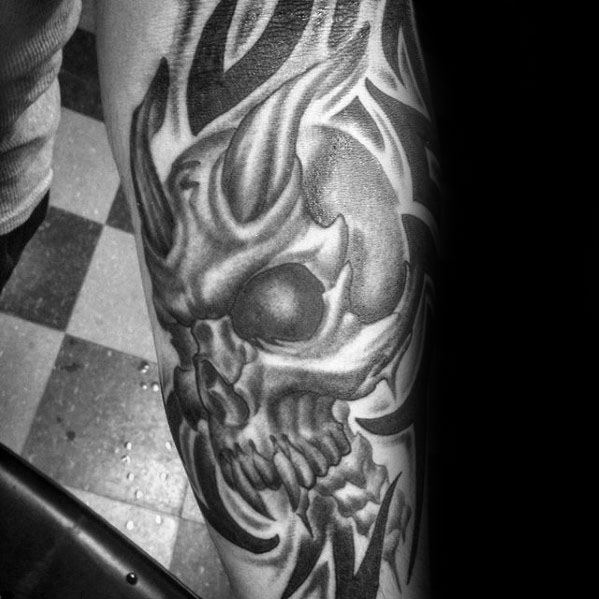 Demonic tribal skull tattoo on forearm with horn-like shapes, dark shading, and intense details creating a fierce, aggressive look.