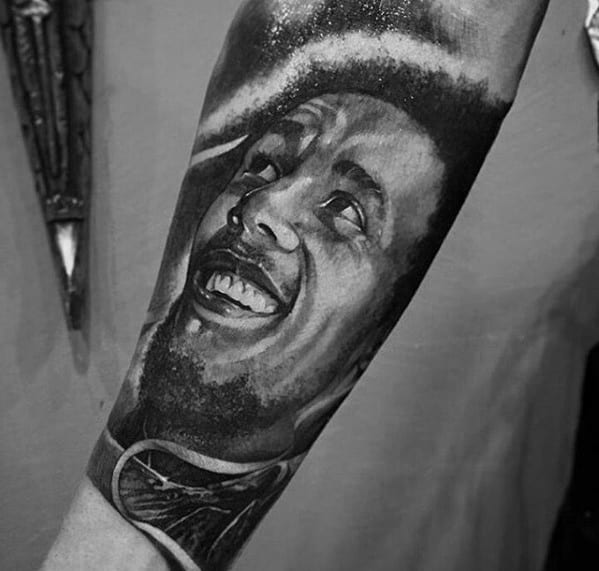 Forearm tattoo of Bob Marley looking upward with a joyful expression, done in black and gray realism with bold contrast and fine detail.
