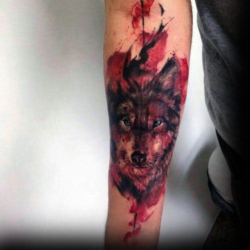Forearm wolf tattoo with piercing eyes, surrounded by intense red and black watercolor splashes for a fierce, dramatic effect.