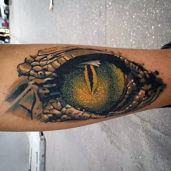 A tattoo of a detailed, yellow-green reptilian eye on a forearm