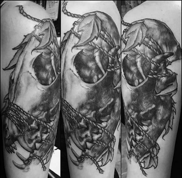 Realistic black and grey tattoo of a fox skull with leaves and rope, featuring deep shading and a dramatic, textured finish.