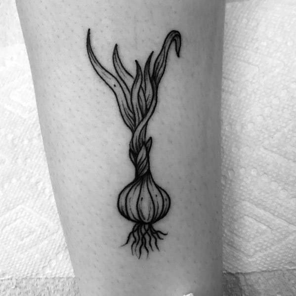 Minimalist garlic tattoo with fine linework, twisted stem, and delicate roots, creating an elegant and organic botanical design on the leg.